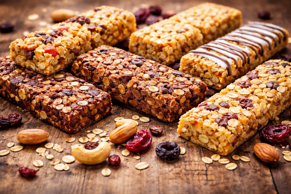 Assorted protein bars with nut fillings displayed on a rustic wooden table with scattered ingredients.